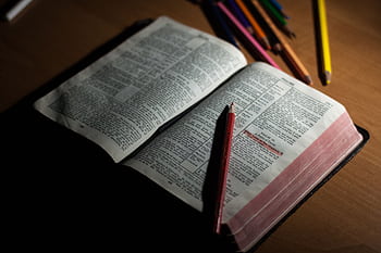 An open Bible on a wooden table accompanied by colored pencils, symbolizing study and spirituality. HD wallpaper