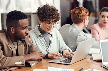 A group of diverse professionals engaged in a team meeting, working on laptops in a modern office setting. HD wallpaper