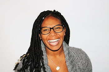 A vibrant portrait of a smiling woman with dreadlocks and glasses, exuding joy. HD wallpaper