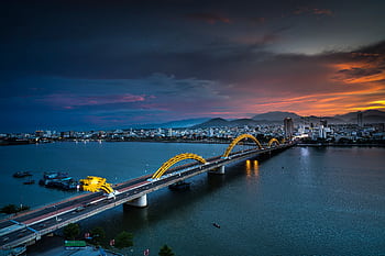 A stunning aerial view of the Dragon Bridge at sunset in Da Nang, Vietnam, highlighting illuminated cityscape. HD wallpaper