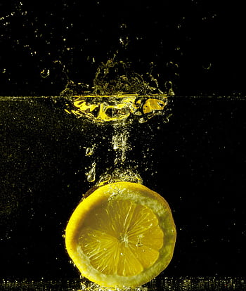 Close-up of a lemon slice creating a splash in water, capturing vibrant colors and lively motion. HD phone wallpaper