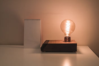 A minimalist setting featuring an Edison bulb lamp and a blank notepad on a white desk, perfect for conceptual ideas. HD wallpaper