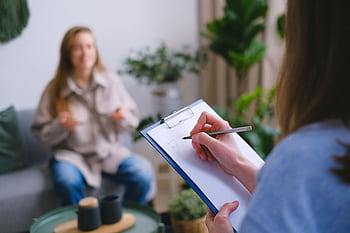A therapist taking notes during a counseling session with a female client in an office. HD wallpaper