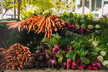 A vibrant display of fresh carrots, radishes, and greens at a local outdoor market. HD wallpaper