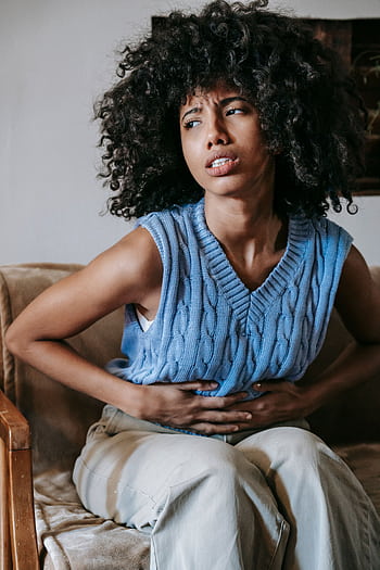 African American woman in pain due to stomach cramps indoors. Health and wellness concept. HD phone wallpaper