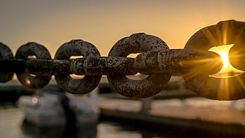 Close-up of a rusty chain with sunrise and water reflections in the background. HD wallpaper