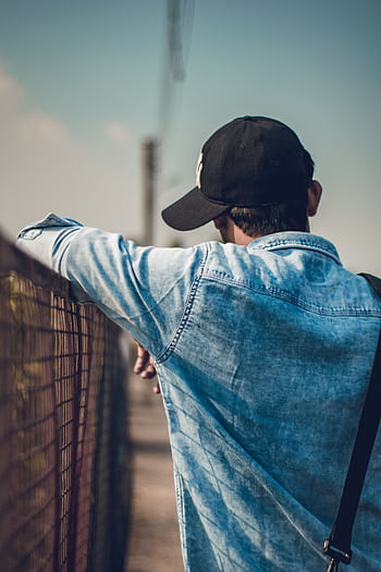 Back view of a man in denim jacket and cap posing outdoors by a fence. HD phone wallpaper