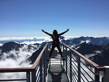 A woman stands on a viewing platform in Vysoké Tatry, Slovakia, surrounded by clouds and mountains, embracing dom. HD wallpaper