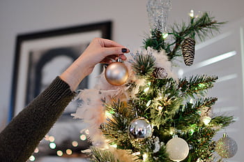 A hand decorates a Christmas tree with shiny ornaments, capturing the festive spirit. HD wallpaper
