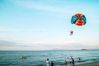 Exciting parasailing experience over the ocean with a vibrant parachute and scenic beach view. HD wallpaper
