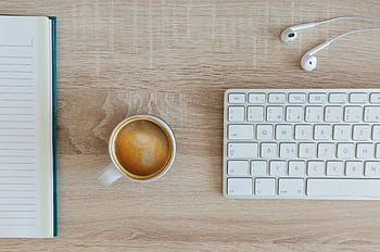 A tidy workspace with a notebook, coffee cup, keyboard, and ears on a wooden desk. HD wallpaper