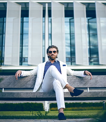 Fashionable man in white suit sitting confidently on a bench outdoors, embodying elegance and modern lifestyle. HD phone wallpaper