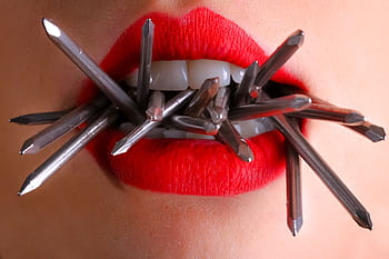 Artistic close-up of red lips biting metal spikes, contrasting beauty and strength. HD wallpaper