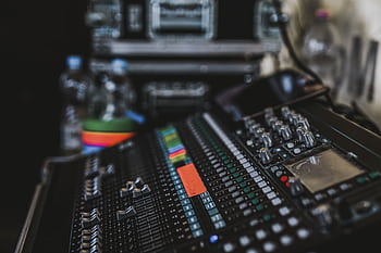 Close-up of a professional audio mixer with various knobs and sliders in a music studio setting. HD wallpaper