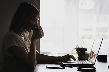 A businesswoman works remotely from home, sipping coffee and using her laptop. HD wallpaper