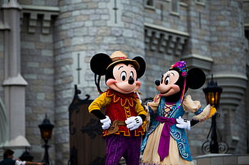 Mickey and Minnie Mouse in colorful costumes outside an iconic castle setting. HD wallpaper