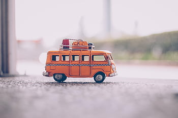 Close-up of a vintage orange toy van with luggage on a textured surface, capturing a nostalgic travel vibe. HD wallpaper