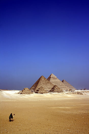 Stunning view of the Pyramids of Giza with a lone figure and camel under a clear blue sky. HD phone wallpaper