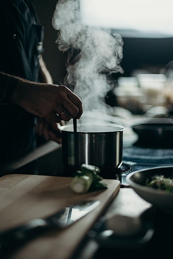 A person stirring a steaming pot on an electric stove with kitchenware spread out. HD phone wallpaper