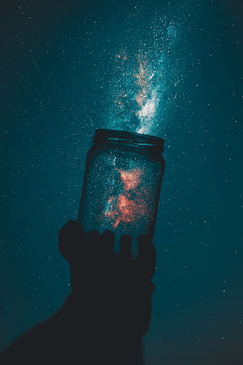 A silhouette hand holds a mason jar capturing a stunning galaxy under a starry night sky. HD phone wallpaper