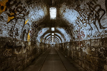 A gritty urban tunnel adorned with graffiti and dim lighting provides a raw, intriguing atmosphere. HD wallpaper