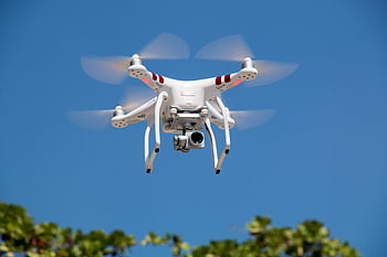 A white drone flying with camera against a clear blue sky in La Libertad. HD wallpaper
