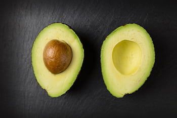 Close-up of fresh sliced avocado halves on a dark slate surface, showcasing healthy eating. HD wallpaper