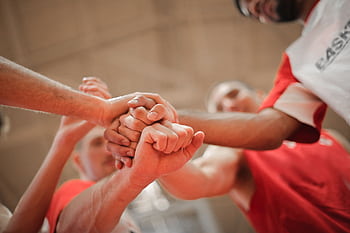 A group of athletes stacking hands, symbolizing unity and teamwork on the basketball court. HD wallpaper