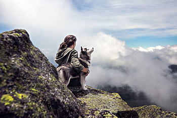 Woman with a husky on a mountain peak overlooking a cloud-filled valley. HD wallpaper