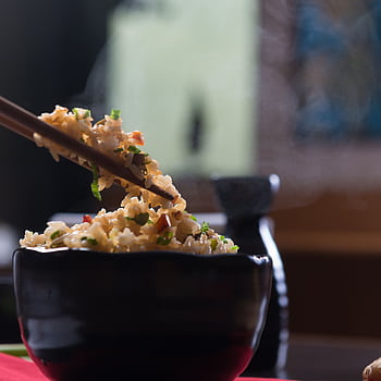 Delicious steaming fried rice in a black ceramic bowl with chopsticks, perfect for an appetizing meal. HD phone wallpaper