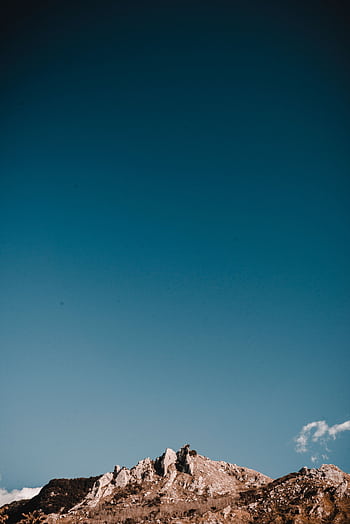 A breathtaking view of a rocky mountain peak with a vast clear blue sky above, perfect for nature-inspired designs. HD phone wallpaper