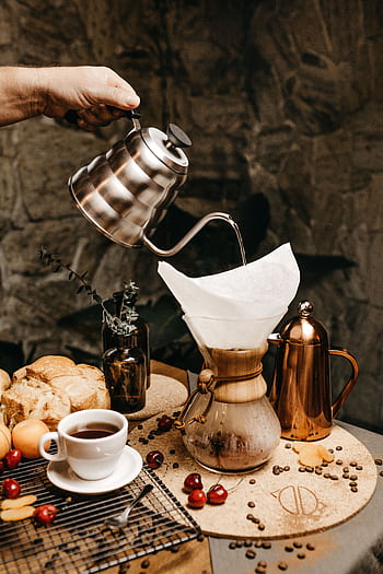 Hand pouring coffee into a Chemex surrounded by fresh cherries and breakfast items indoors. HD phone wallpaper