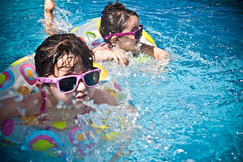 Two young girls enjoying a playful day in a bright blue swimming pool with colorful float rings. HD wallpaper