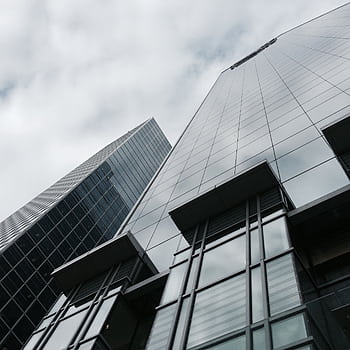 Low angle view of two modern skyscrapers with glass facades against a cloudy sky. HD phone wallpaper