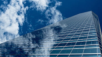Low-angle view of a modern skyscraper with reflective glass windows against a blue sky. HD wallpaper