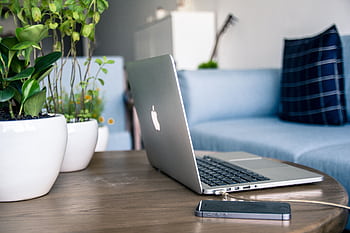A contemporary home office setup featuring a sleek laptop, smart, and potted plants on a wooden table. HD wallpaper