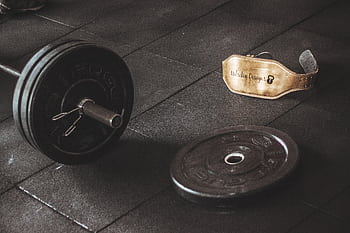 A heavy barbell and weightlifting belt on a gym floor, emphasizing strength and fitness. HD wallpaper