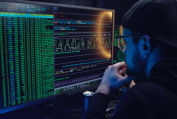 Man intently working on computer programming with code displayed on dual monitors in a dimly lit room. HD wallpaper