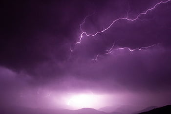 Captivating shot of lightning illuminating a stormy purple sky over a mountainous landscape. HD wallpaper