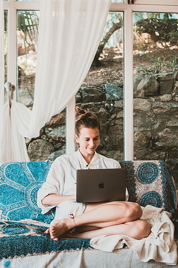 A woman sitting comfortably on a sofa using a laptop, depicting a serene remote work setup. HD phone wallpaper