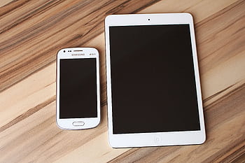 A white smart and tablet placed on a wooden table, showcasing technology contrast. HD wallpaper