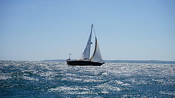 A sailboat gracefully navigates the sparkling ocean off the coast of Cornwall on a sunny summer day. HD wallpaper