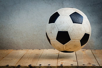 Vintage soccer ball resting on wooden planks against a textured background, symbolizing sports tradition. HD wallpaper