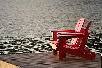 Two red Adirondack chairs on a wooden dock overlooking peaceful waters, ideal for relaxation. HD wallpaper