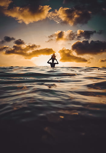 A silhouette of a person enjoying the ocean at sunset, capturing serene beauty. HD phone wallpaper
