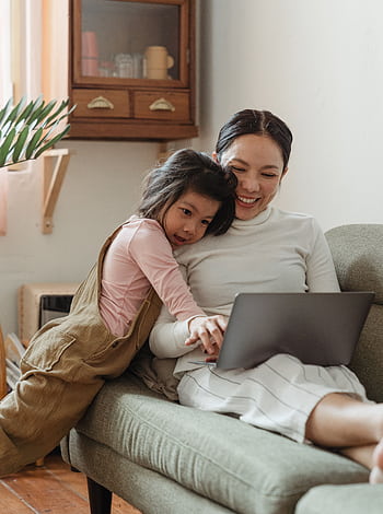 A joyful mother and daughter bonding while using a laptop in a cozy living room. HD phone wallpaper