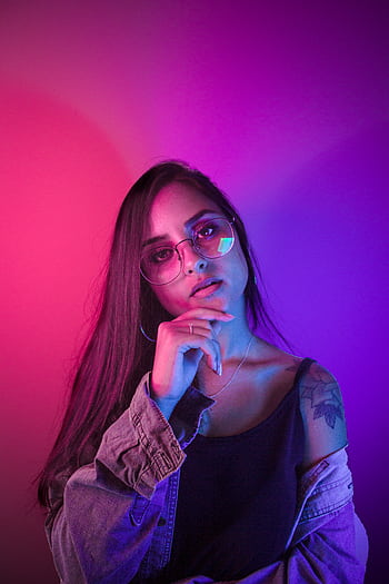 Stylish woman in neon lighting, wearing glasses and denim, posing confidently. HD phone wallpaper