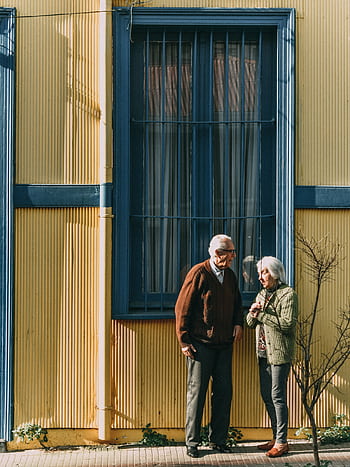 A senior couple standing in front of a colorful building in Valparaíso, enjoying the sunny day. HD phone wallpaper