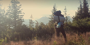 A lone hiker with a backpack and sleeping mat in a sunny mountain landscape. HD wallpaper