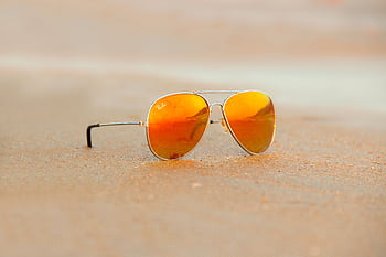 Close-up of aviator sunglasses on sand with orange reflection, evoking a warm summer vibe. HD wallpaper